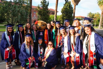 Image of graduates in their cap and gown posing with Wilma Wildcat